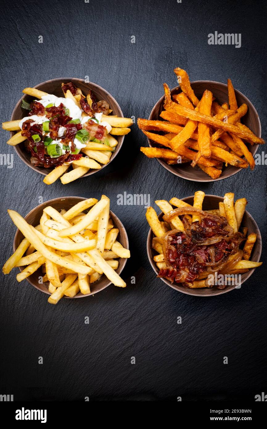 Four different fries with different sauce with onion or bacon sauce, arranged in identical bowls on a black skipper plate Stock Photo