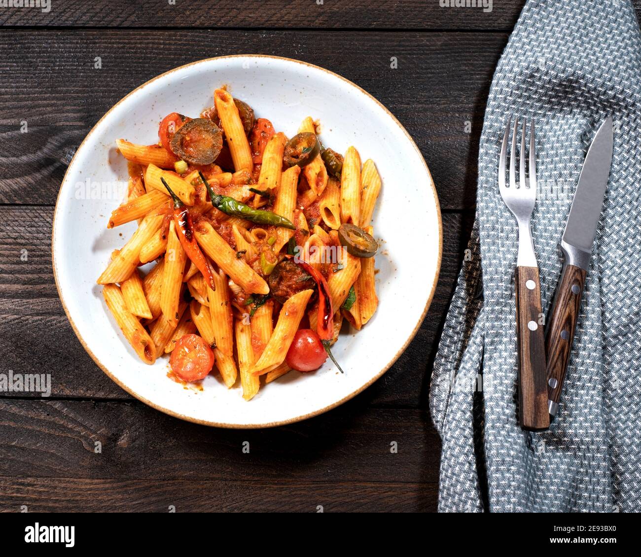 Rigatoni arrabiata with fiery tomato sauce on a brown wooden table with a fork and a knife Stock Photo