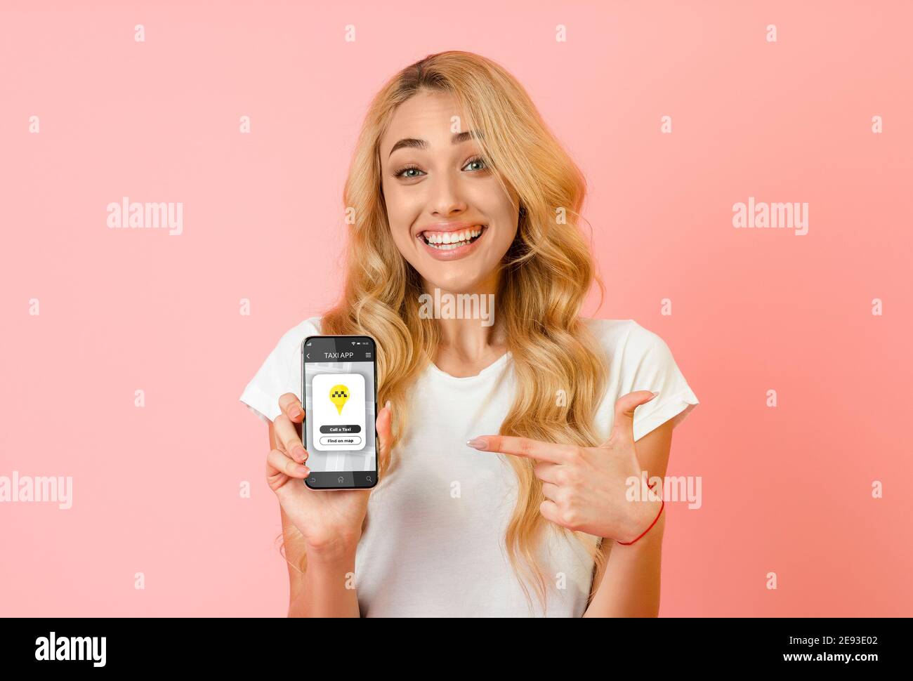 Happy woman pointing at smartphone with mobile taxi app on screen over pink studio background. Urban transport concept Stock Photo
