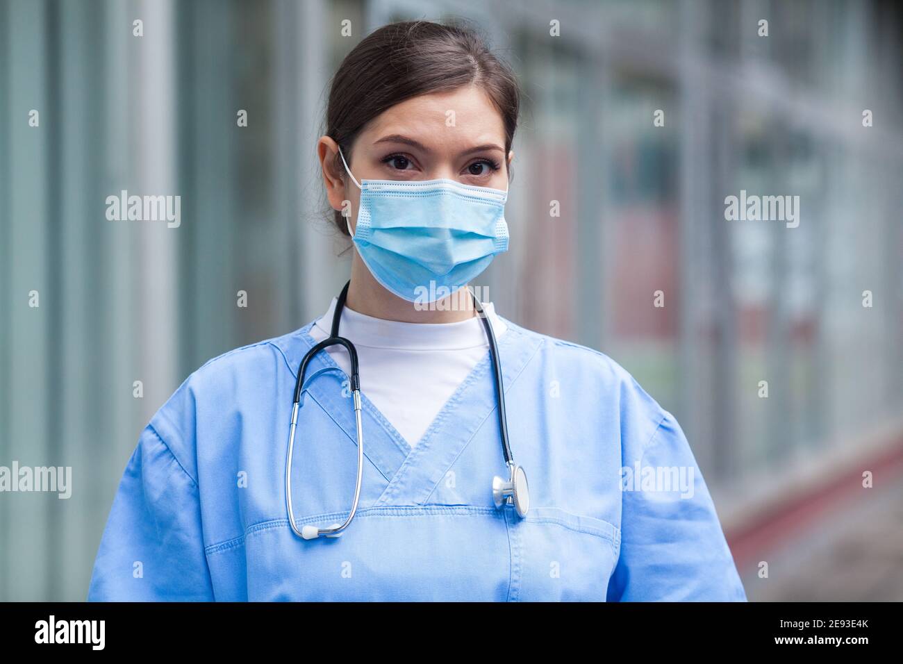 Young worried stressed anxious female EMS key worker doctor,unhappy portrait in front of UK NHS healthcare ICU facility,GP wearing protective PPE face Stock Photo