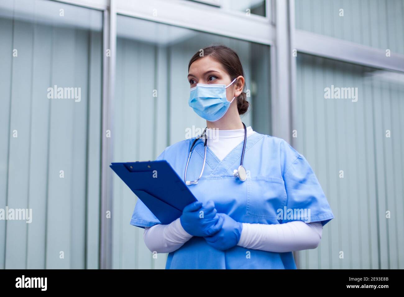 Female UK NHS ICU medical worker,woman doctor holding clipboard wearing PPE blue protective scrubs face mask,front line emergency medic,COVID-19 pande Stock Photo