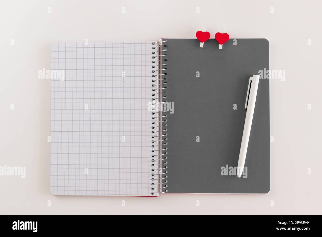 Opened spiral notebook with gray sheet with with two heart shaped clothespins and white pen on white background. Mock up for Valentine day, love and r Stock Photo