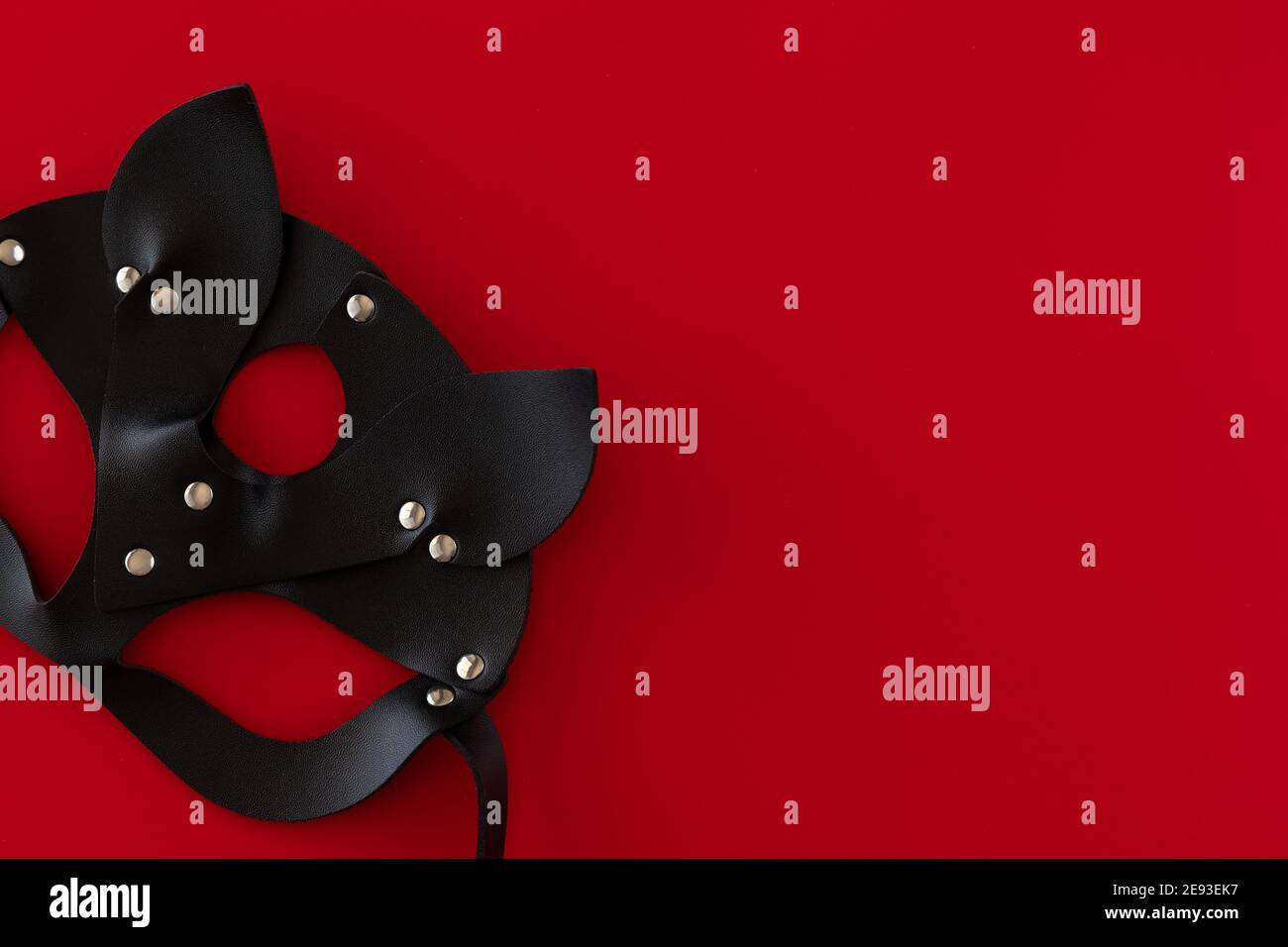 Black leather sexy cat mask on a red background with space for text. Concept of Valentine's Day. Copy space, top view. The concept of Valentine's Day. Stock Photo