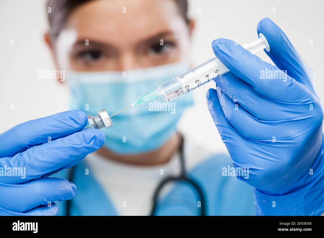 UK NHS young caucasian female GP doctor holding syringe,injecting needle in ampoule vial,COVID-19 vaccine illustration,potential cure for global Coron Stock Photo