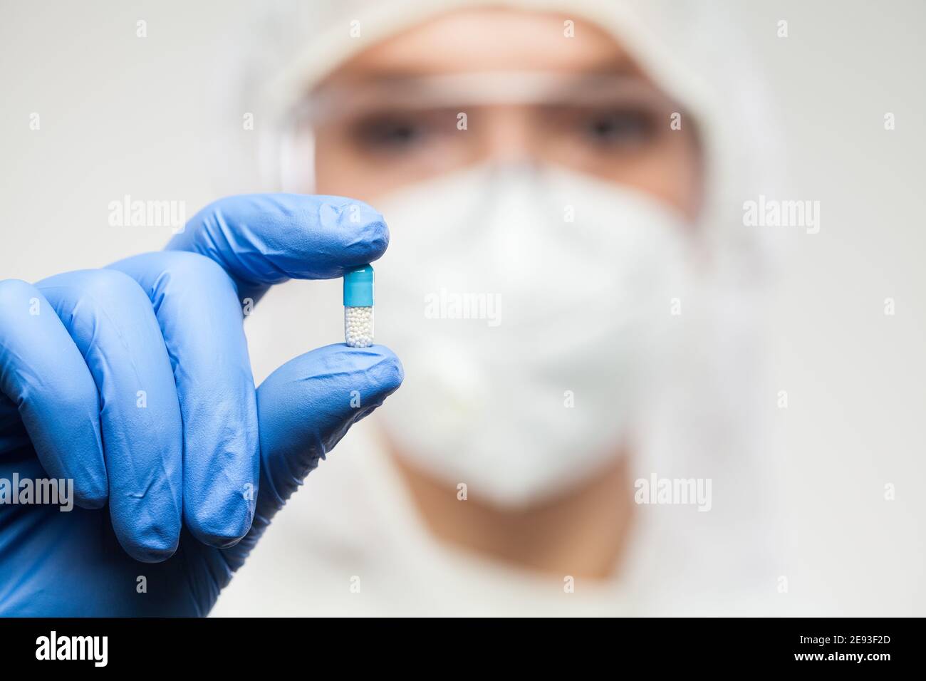 Female UK NHS pharmacist wearing PPE personal protective equipment,coveralls,face mask,eyewear,glove,holding blue pill,selective focus,patient cure re Stock Photo