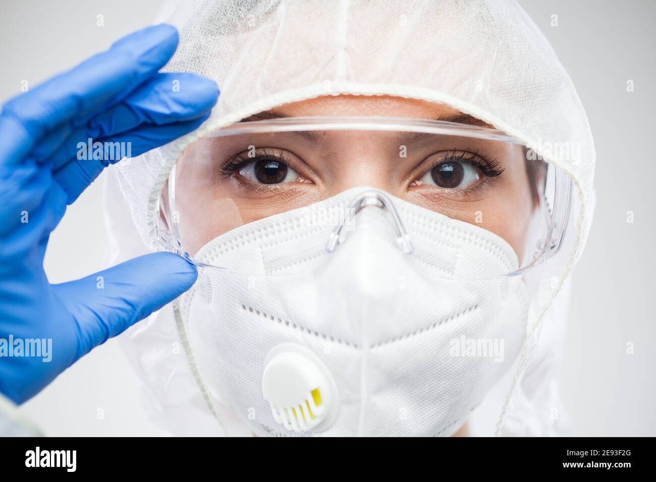 Female lab scientist,doctor or nurse,putting protective eyewear goggles,wearing blue gloves,N95,PPE clean suit,portrait of UK NHS front line medical s Stock Photo