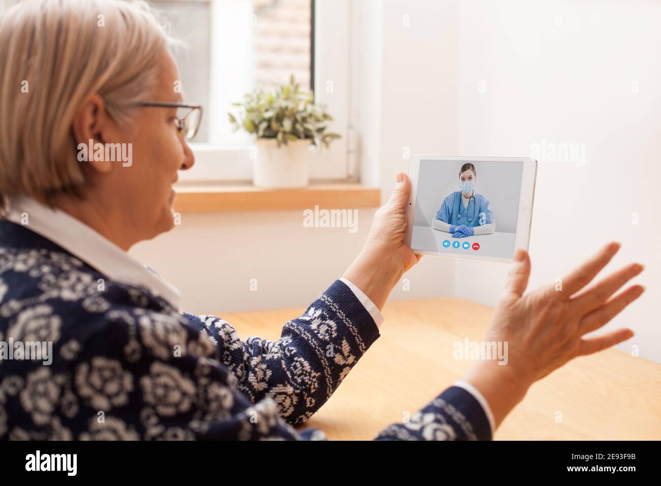 Elderly caucasian woman talking to young female UK e-doctor via online video chat,medical worker seeing patient in virtual house call,telemedicine dur Stock Photo