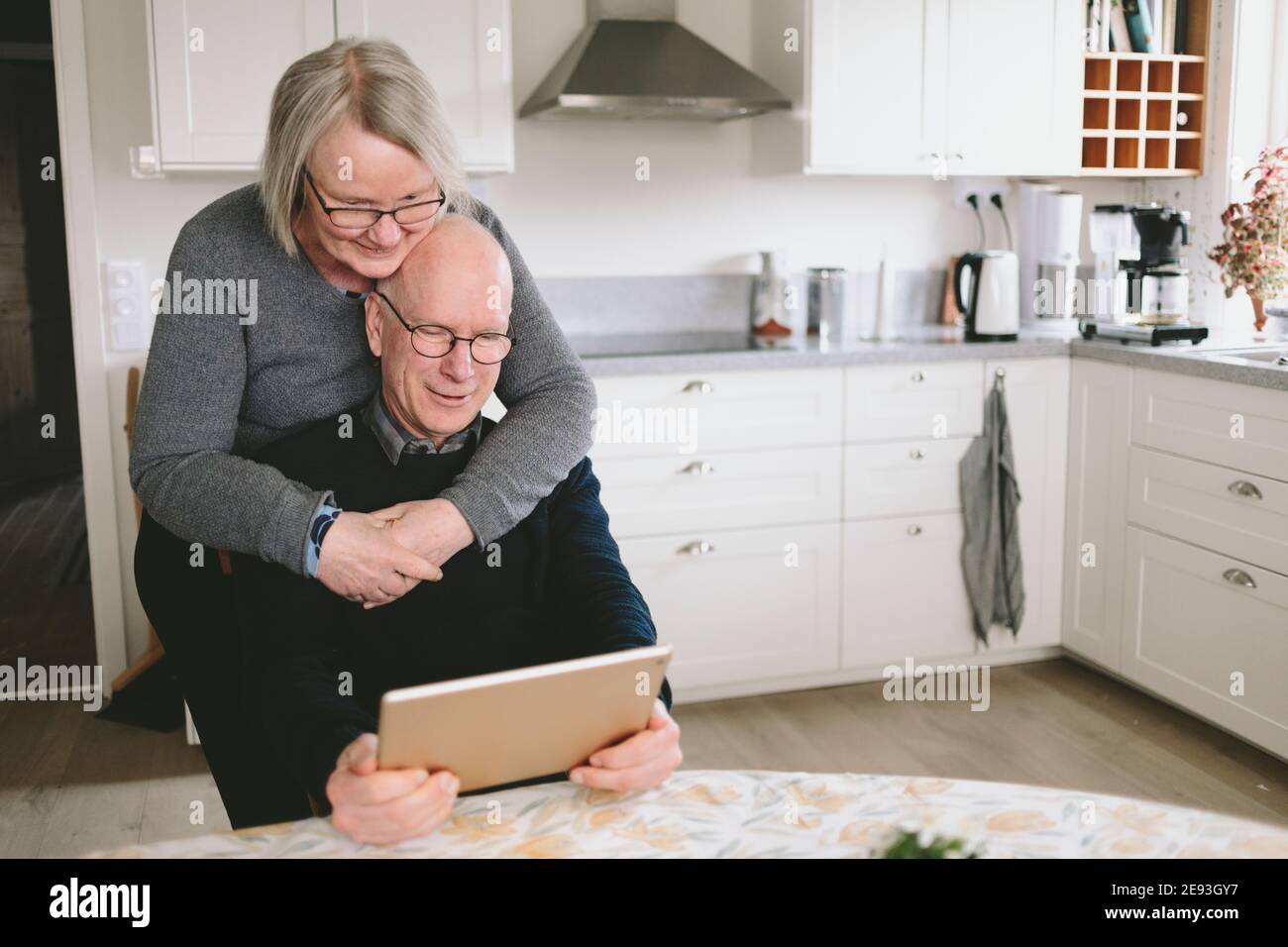 Smiling couple embracing and using tablet at kitchen table Stock Photo