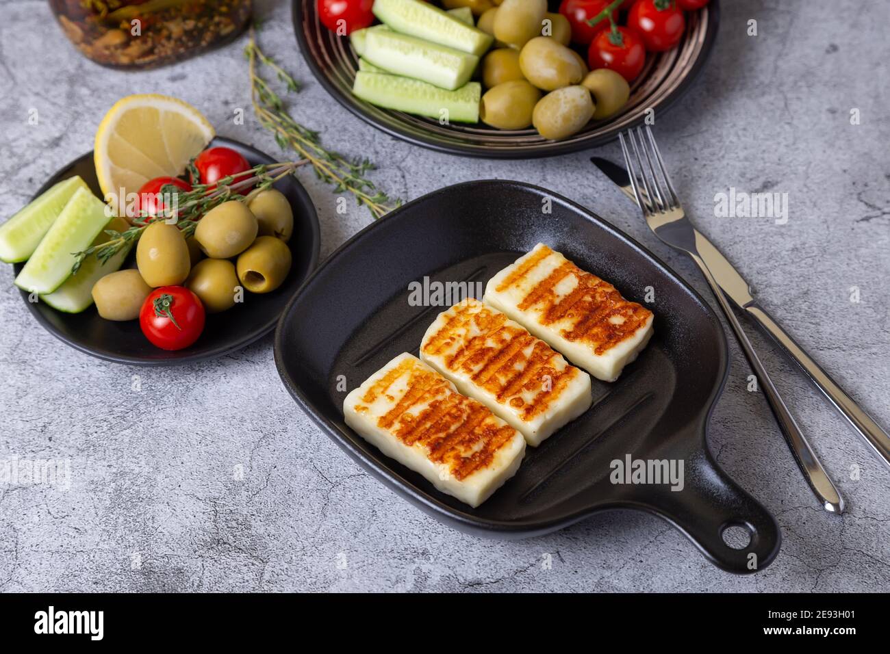 Grilled haloumi cheese on a black pan with olives, tomatoes, cucumbers and pepperoni. Close-up. Stock Photo