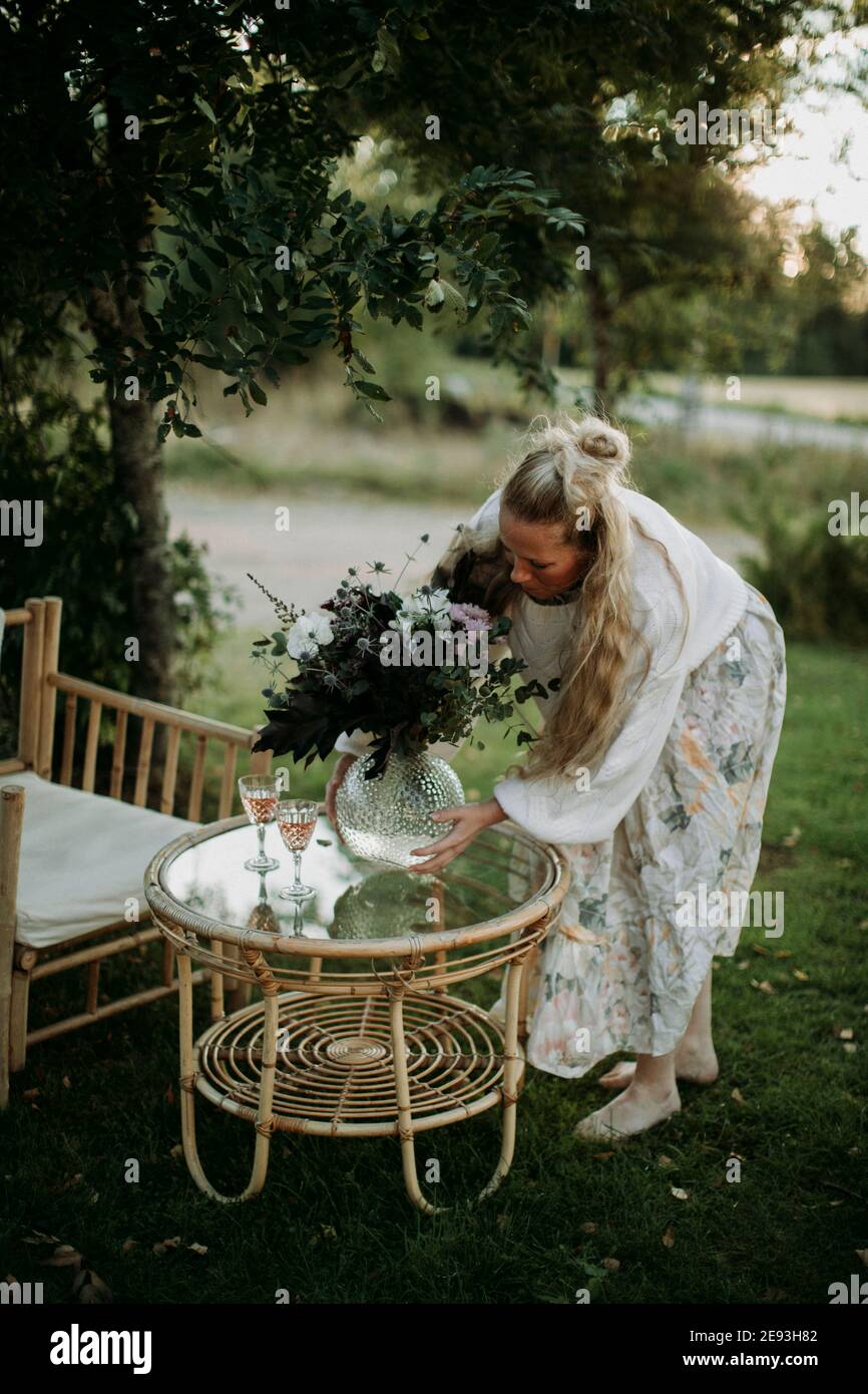 Woman putting vase with flowers on table in garden Stock Photo