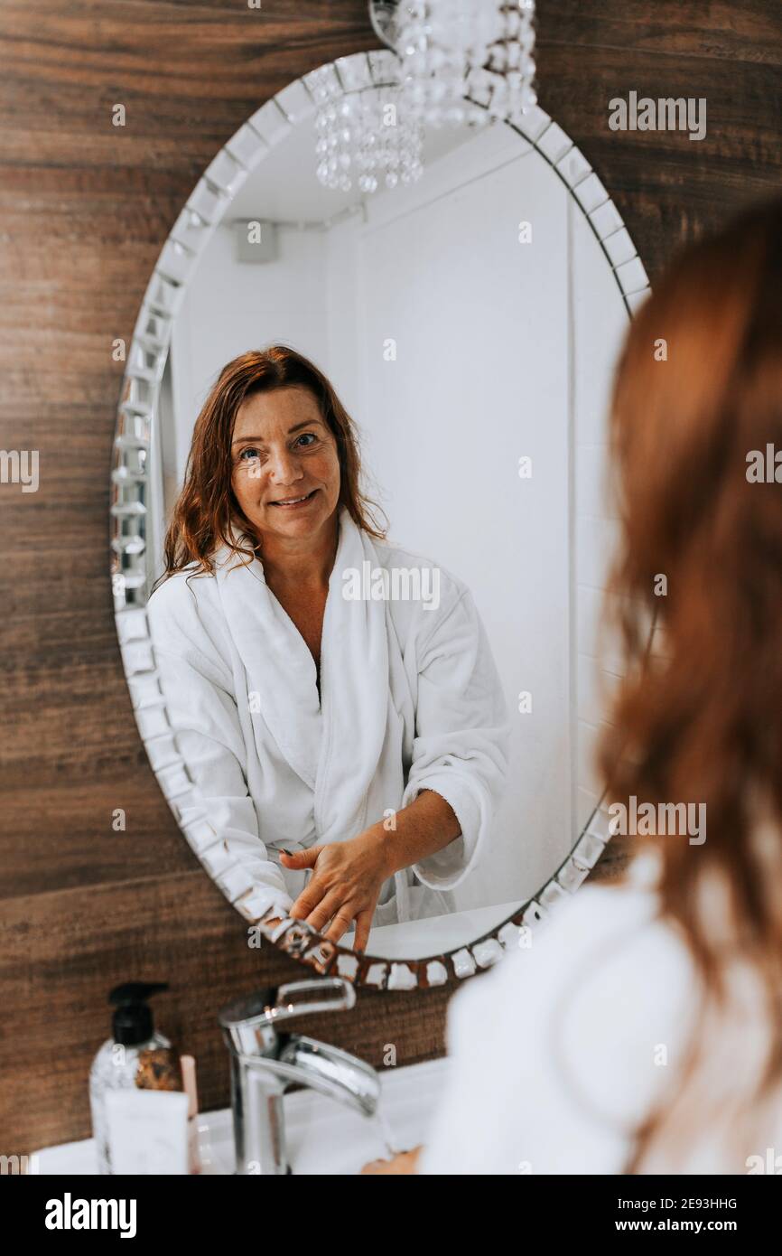 Mature woman reflecting in bathroom mirror Stock Photo