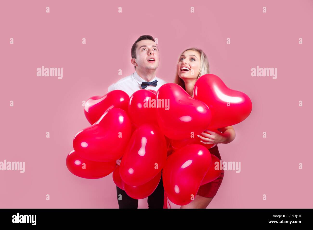 Valentines day. Surprised young couple with balloons heart on pink ...