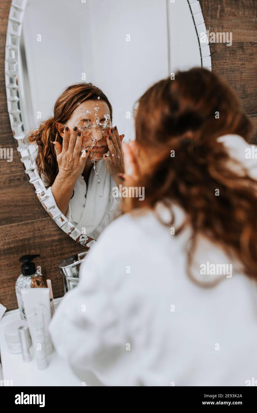 Woman washing her face in front of mirror Stock Photo