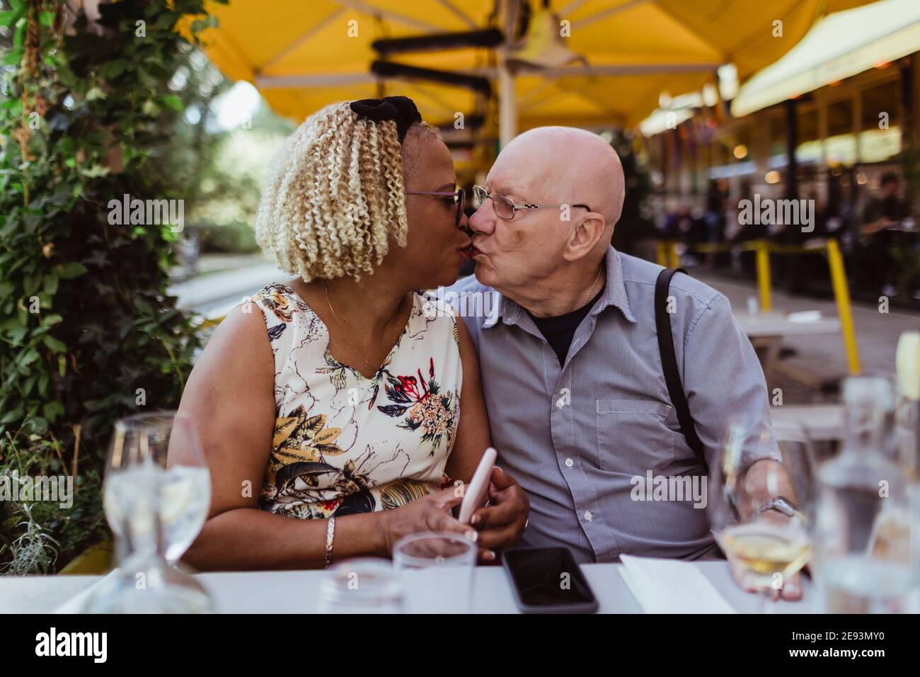 Senior couple kissing each other while sitting at sidewalk cafe Stock Photo
