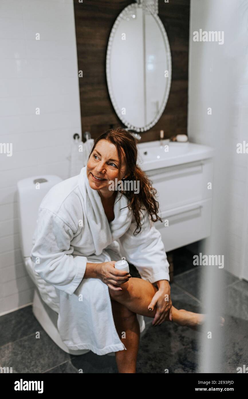 Woman in bathroom applying cream Stock Photo