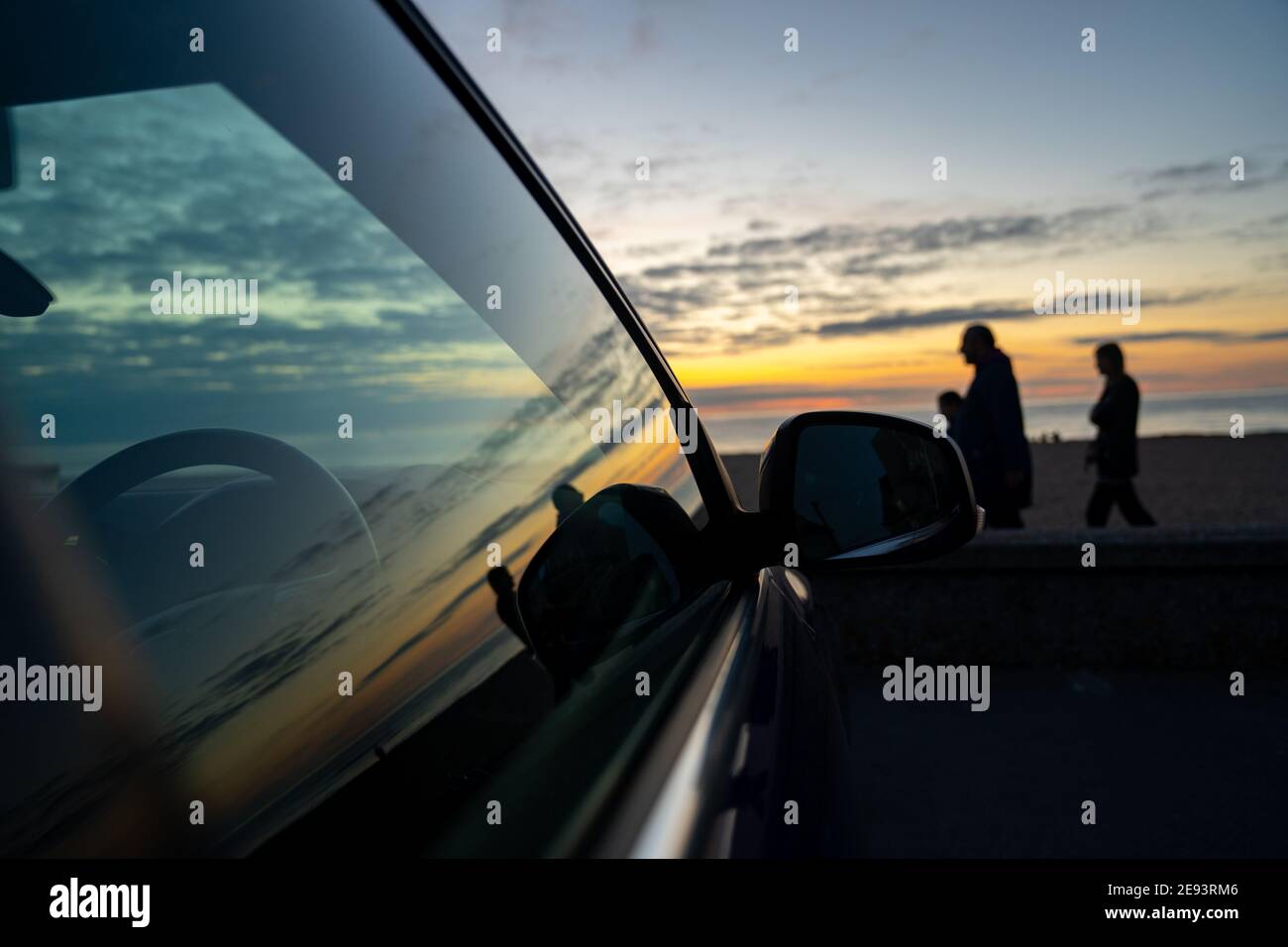 Summer sunset at seaside beach whilst on holiday vacation reflecting in side of car window glass with silhouette of family people walking beautiful Stock Photo