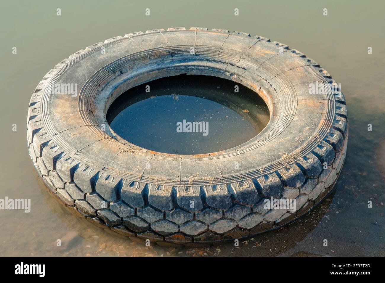An old car tire is lying in the river. Environmental problems, water