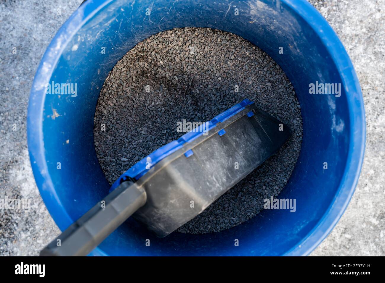 Blue bucket with gravel for icy roads and sidewalks. Shallow field of view. Stock Photo