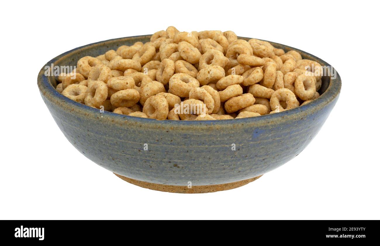 Side view of dry generic round whole grain oat cereal in an old blue stoneware bowl isolated on a white background. Stock Photo
