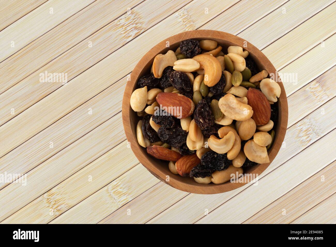 Top view of an assortment of nuts and dried fruit in a wood bowl atop a wood placemat. Stock Photo