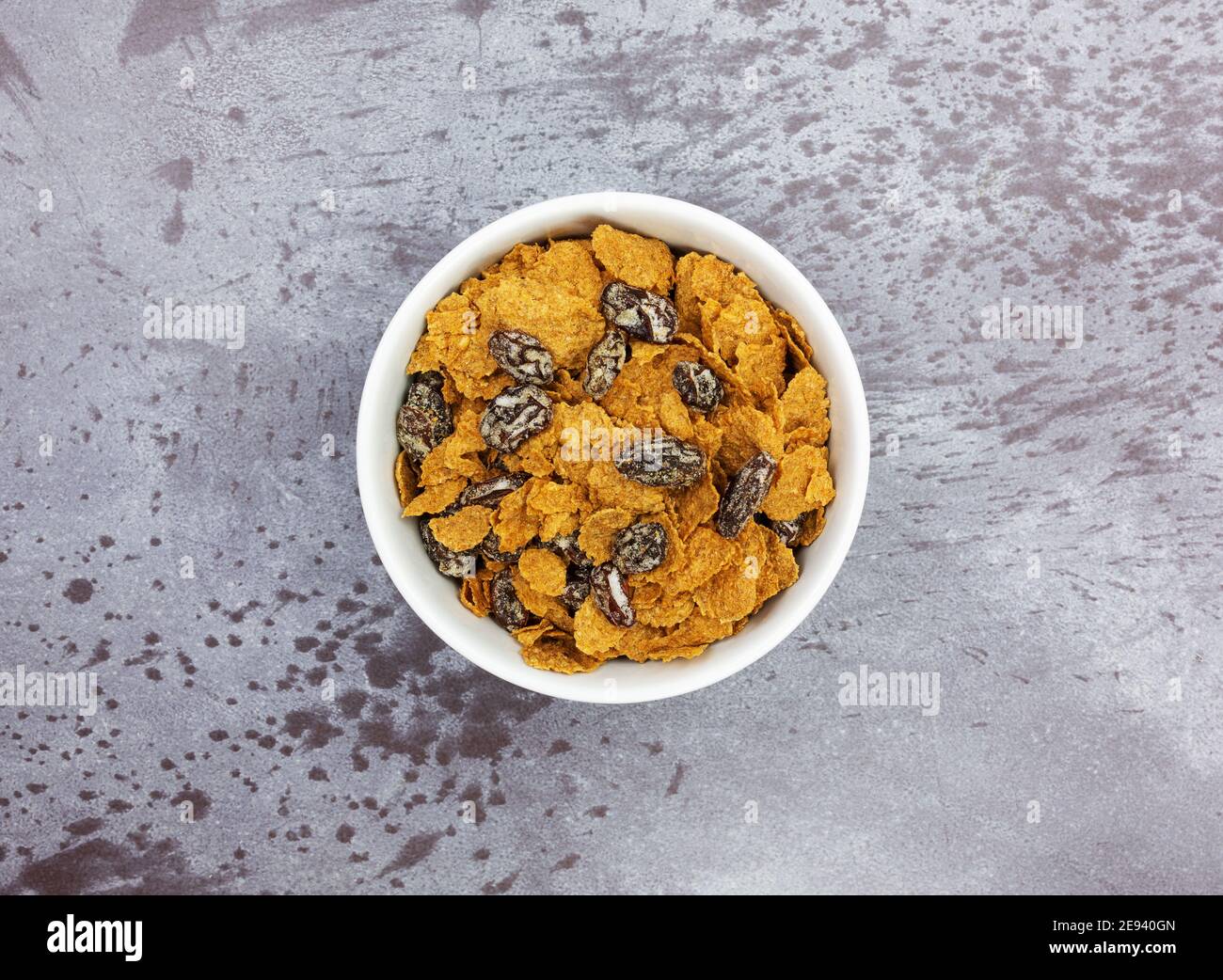 Top view of a white bowl filled with bran flakes and raisins breakfast cereal on a gray background. Stock Photo