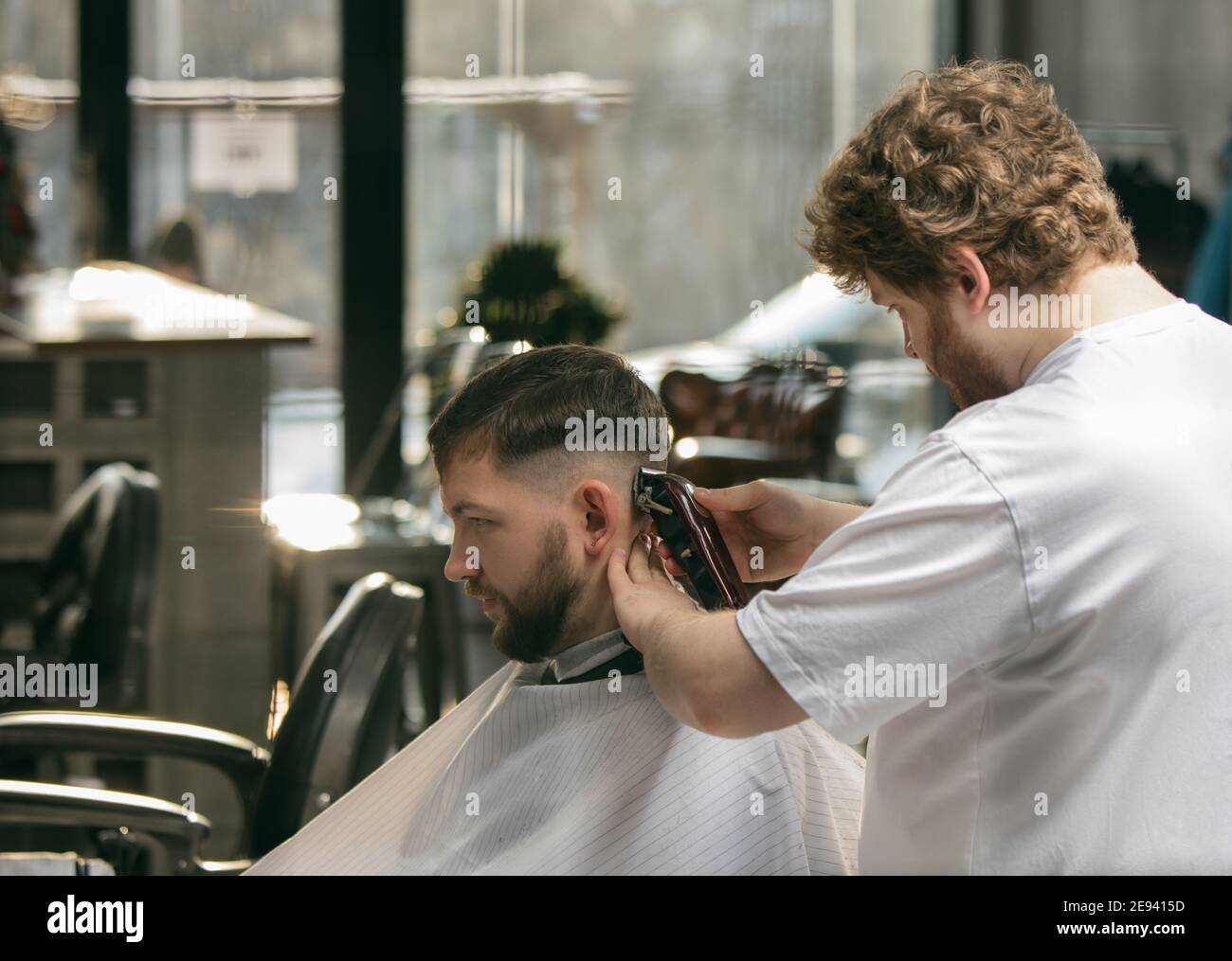 Close up master barber, stylist does the hairstyle to guy, young man