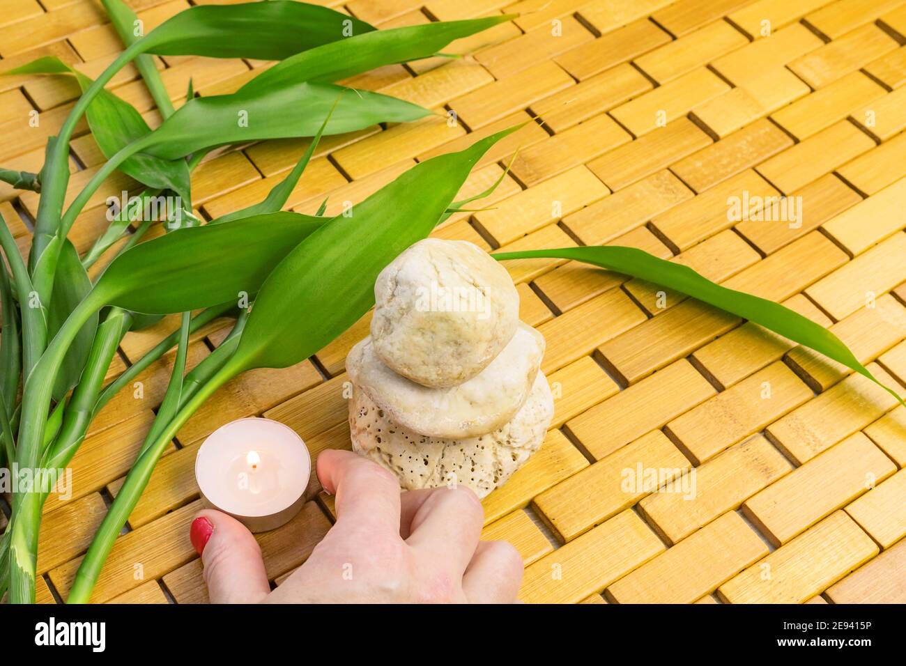 Spa, zen, massage concept. Woman hand holding lighting candle, bamboo leaves and white stone pyramid Stock Photo