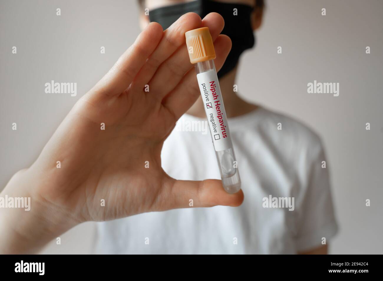 Nipah virus. Young woman wearing a medical face mask holding a glass test tube. Nipah Henipavirus is a newly emerging bat-borne virus that causes acut Stock Photo