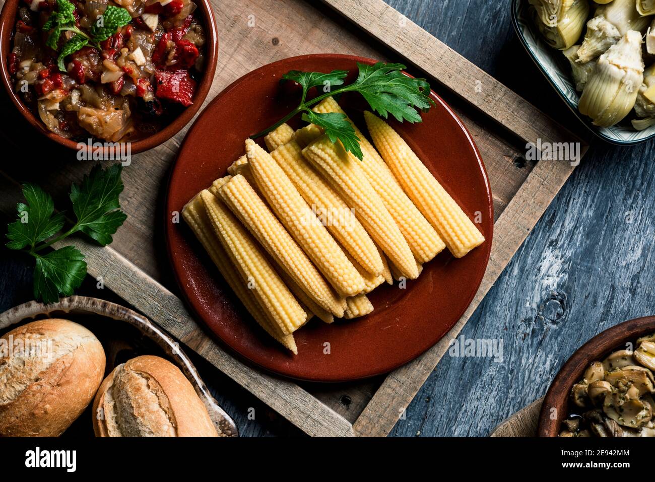 high angle view of some cooked baby corns in a plate on a table next to a bowl with some spanish escalivada, made with different roasted vegetables, s Stock Photo