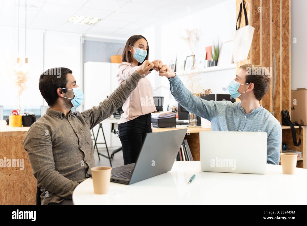 Coworkers wearing face masks celebrating and fist bumping. Working in the office during Coronavirus pandemic concept. Stock Photo