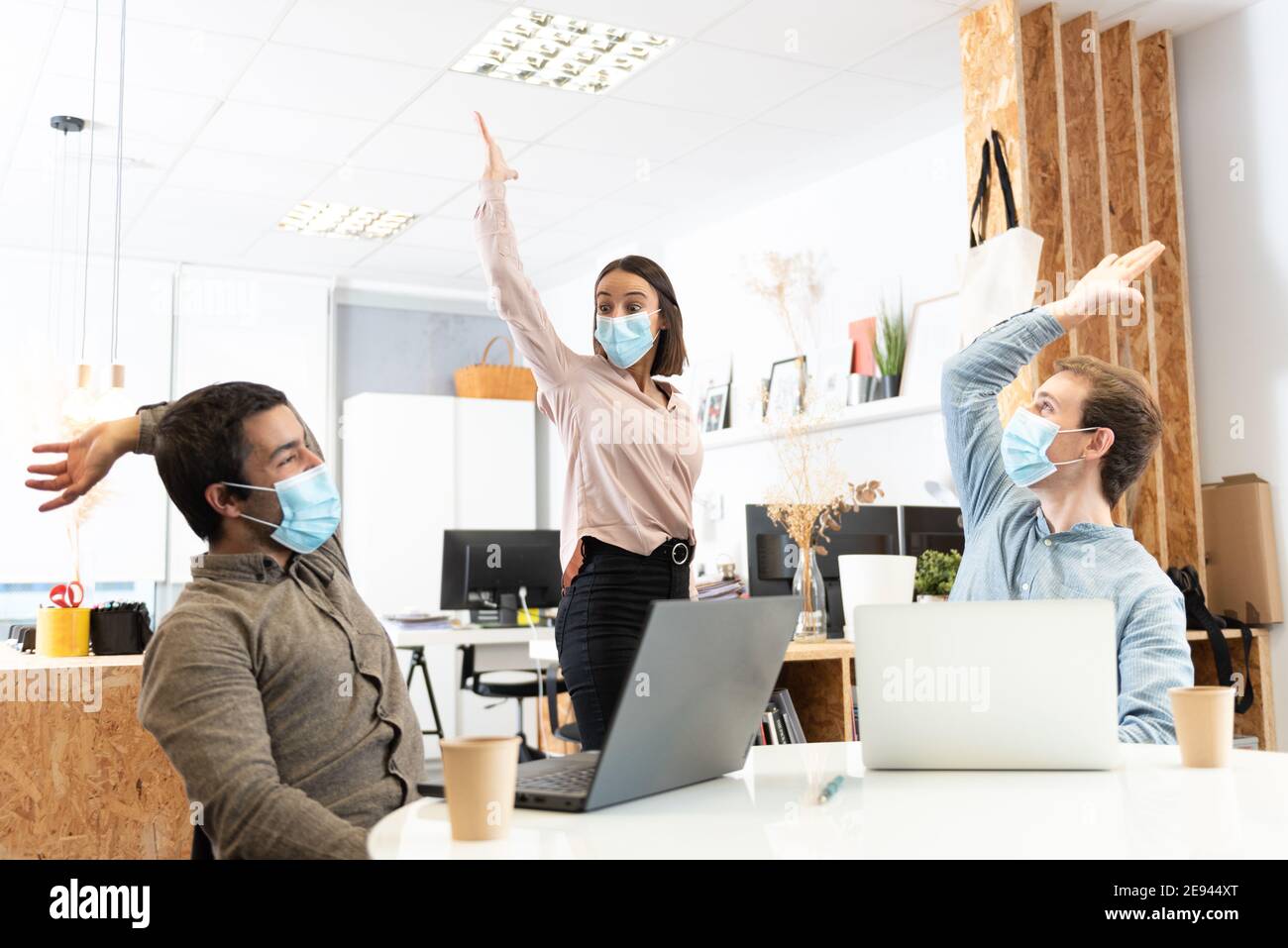 Happy coworkers celebrating with the hands up while wearing protective masks. Working in the office during Coronavirus pandemic concept. Stock Photo