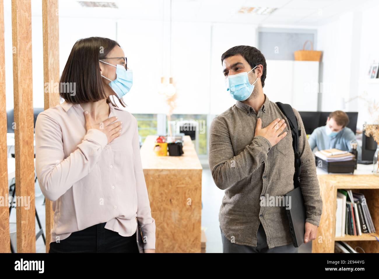 Hispanic coworkers greeting with the hand on chest. Working in the office during Coronavirus pandemic concept. Stock Photo