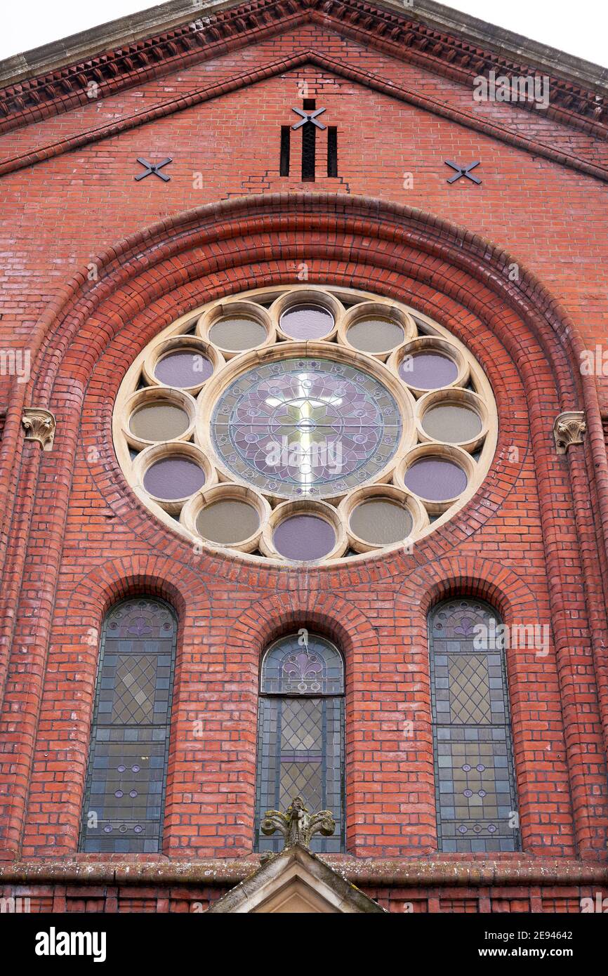 Cross in the centre of an ornate circular window in a red brick church Stock Photo