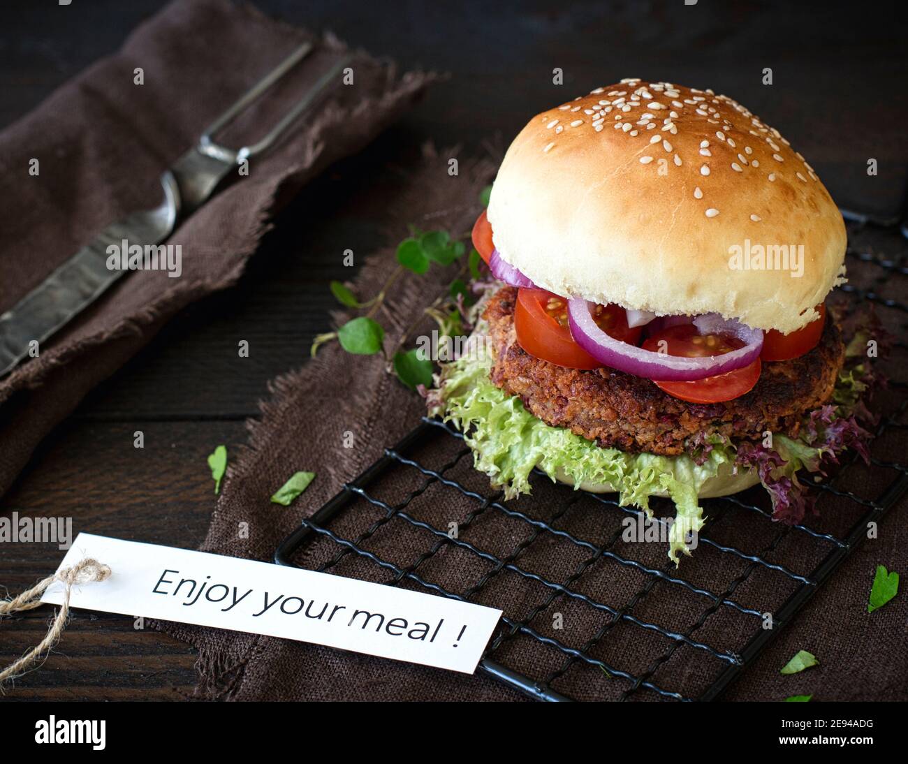 Homemade vegetarian cheese burger on a dark wooden board on a dark brown wooden table, with frensh fries, next to it a brown linen napkin, next to it Stock Photo
