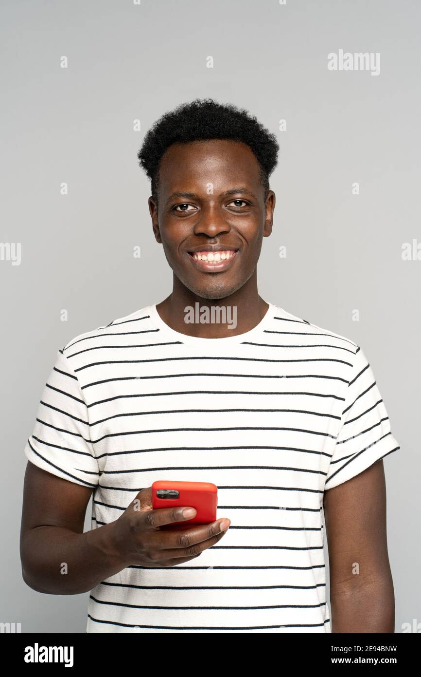 Happy African millennial man in glasses, holding mobile phone, isolated on studio grey background Stock Photo