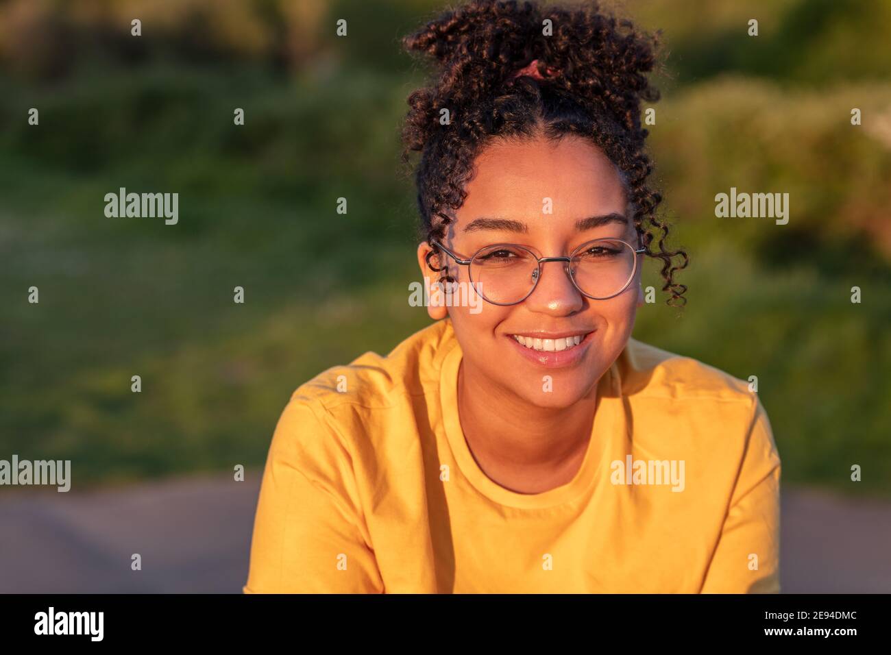 Beautiful biracial mixed race African American teenager teen girl young woman smiling with perfect teeth wearing glasses outside at sunset or sunrise Stock Photo