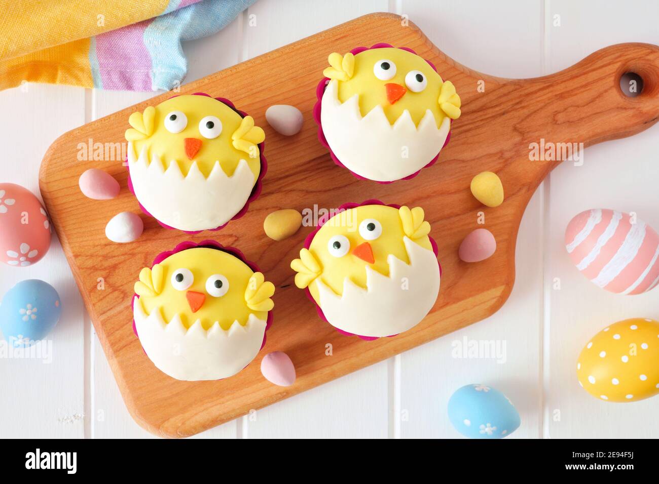 Hatching spring chick cupcakes on a wood paddle board. Flay lay against a white wood background. Stock Photo