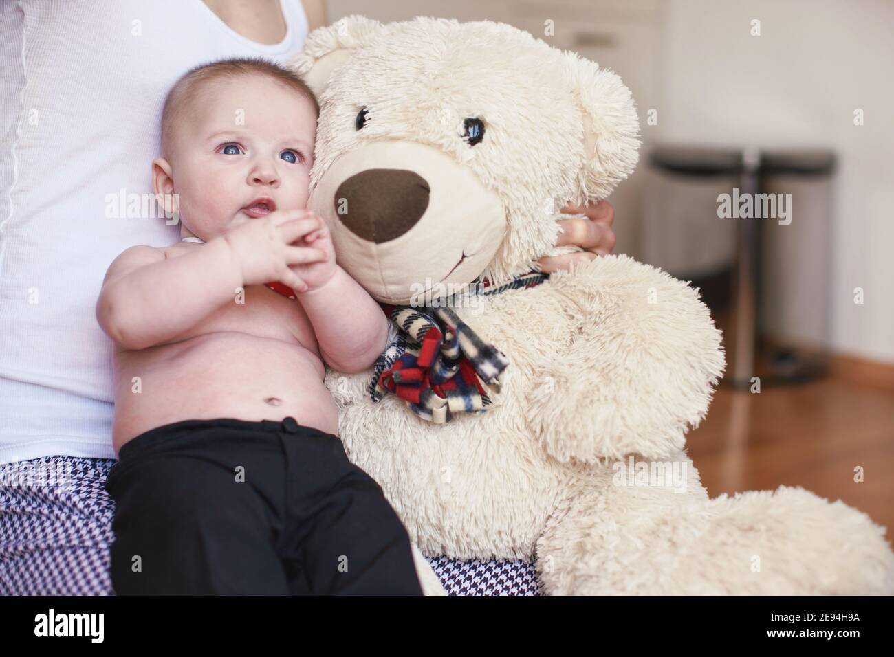 Four months old baby boy sitting on her mother knees, large plush teddy