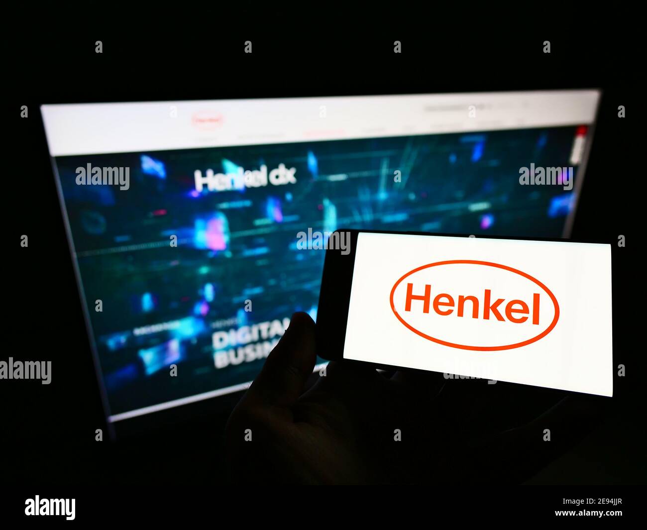 Person holding cellphone with logo of German chemical and consumer goods company Henkel  on display in front of web page. Focus on phone screen. Stock Photo