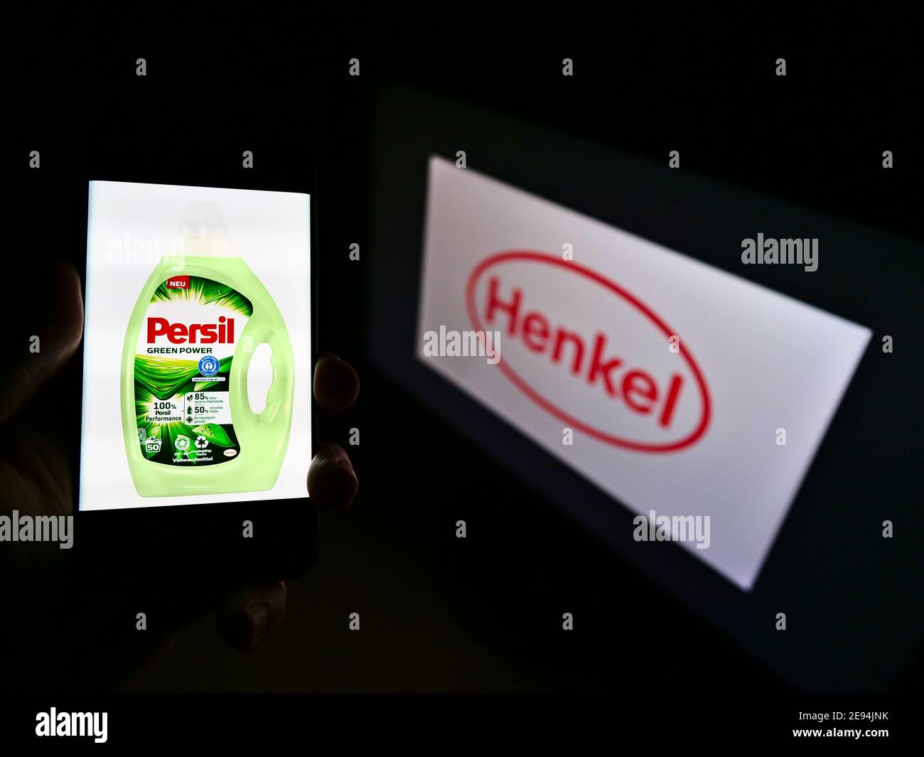 Person holding smartphone with laundry detergent product Persil on display marketed by company Henkel with logo in background. Focus on phone screen. Stock Photo