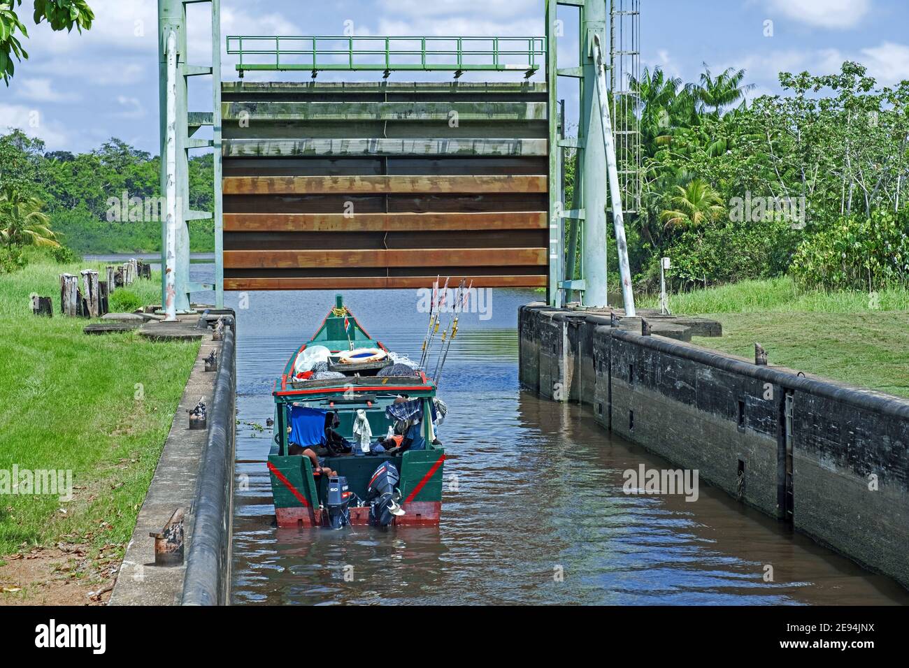 Small traditional wooden fishing boat leaving lock / sluice gate on the Saramacca River at the village Uitkijk, Saramacca District, Suriname / Surinam Stock Photo
