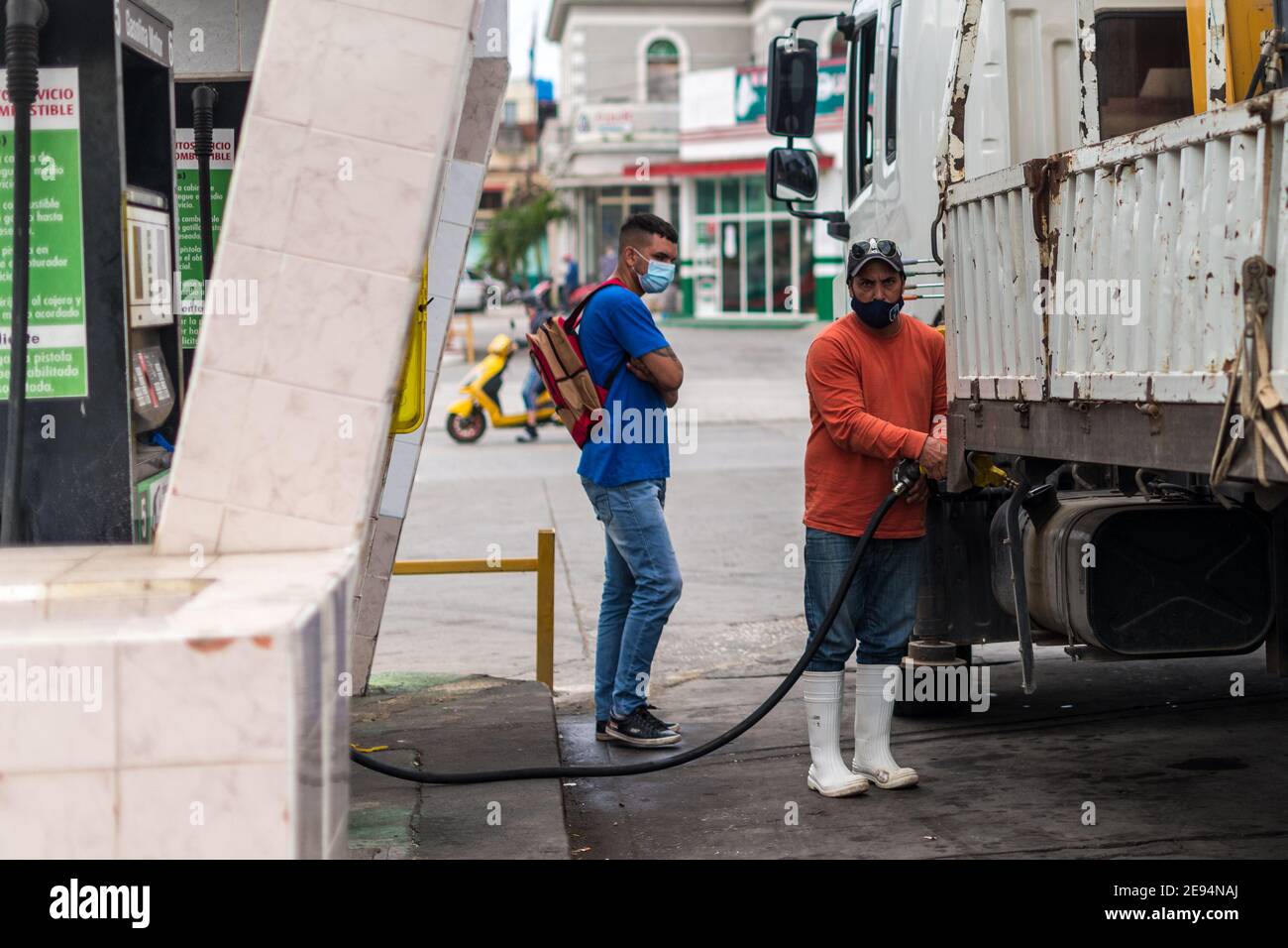 Cuban driver pours fuel to his truck in a garage. He is wearing face masks as it is the time of the Covid-19 Stock Photo