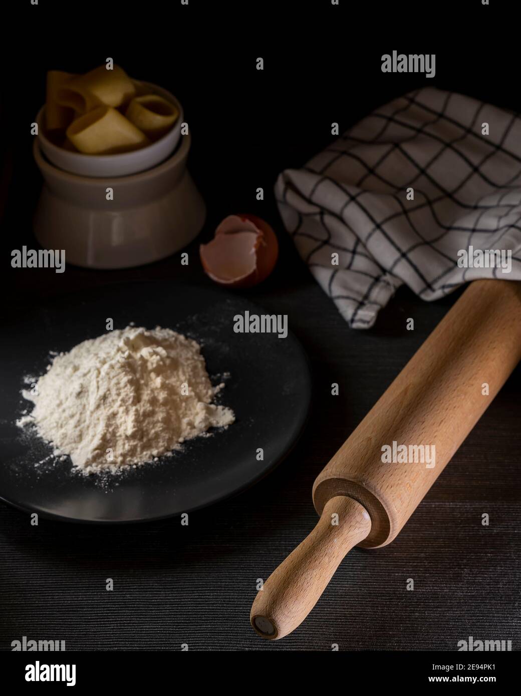 Dark composition of elements for the preparation of homemade pasta such as flour, eggs, wooden rolling pin and various accessories Stock Photo