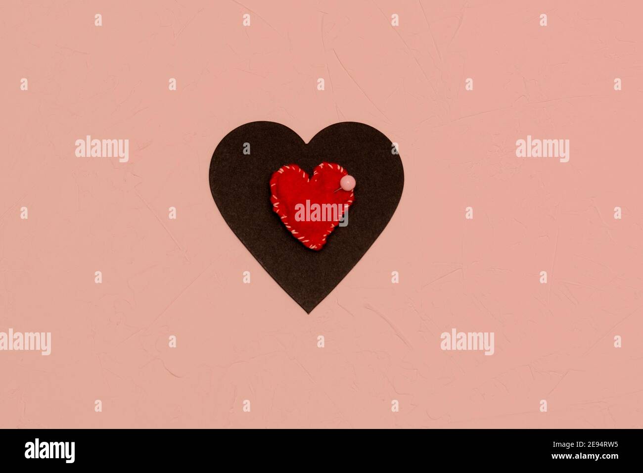 Red heart sewn with threads pinned to black one with needle. Bad love, affection concept. Pink textured background. Stock Photo