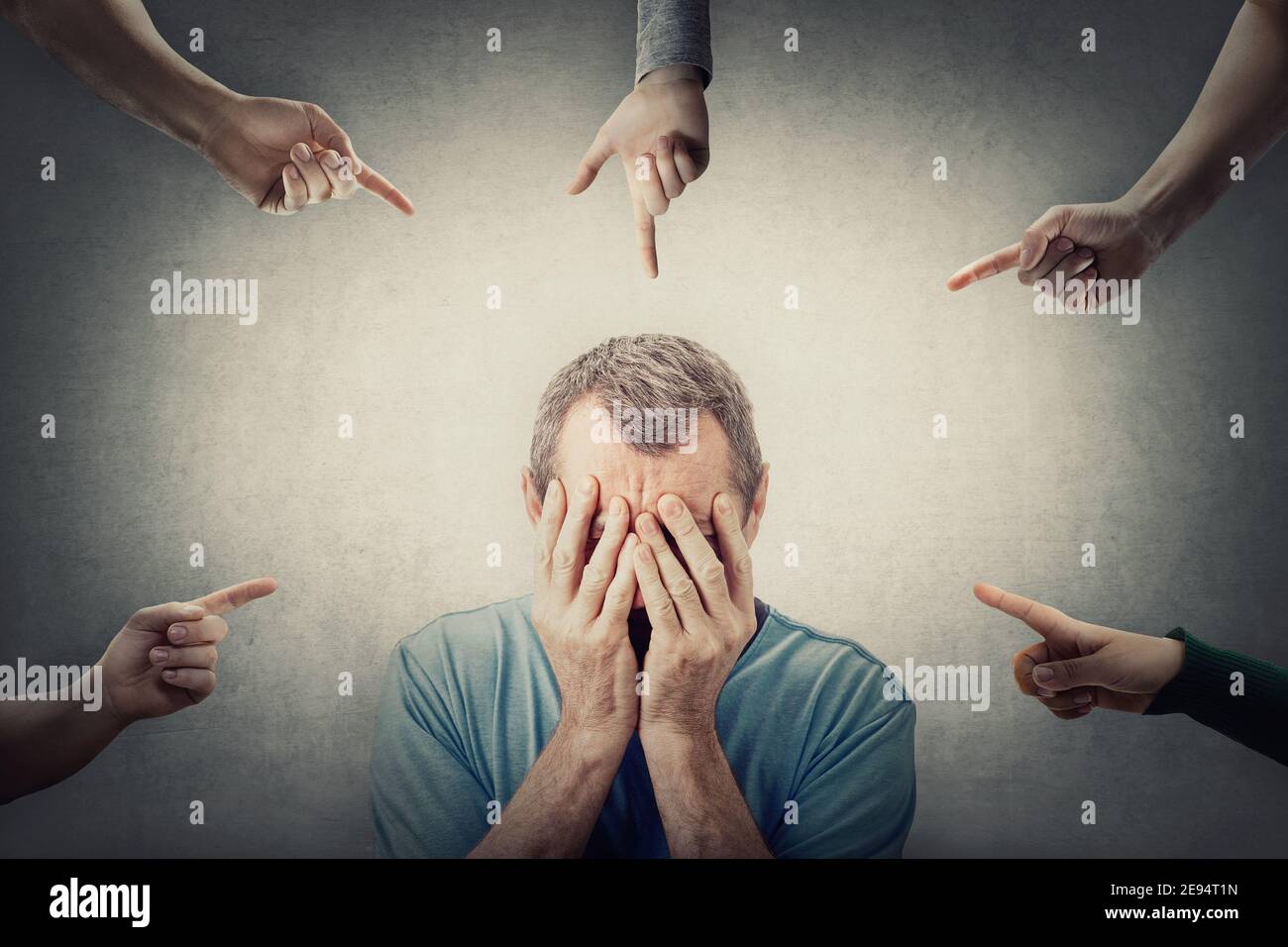 Ashamed middle aged man, covers his face with hands, as multiple people points fingers to him, blaming and scolding. Male senior suffering emotional b Stock Photo
