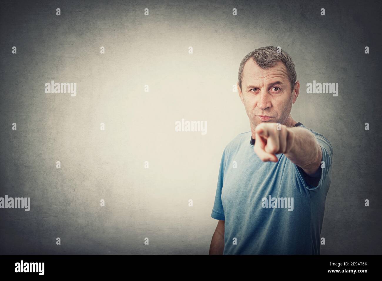 Confident and determined middle age man pointing index finger to camera, like blaming or accuse someone, isolated on grey wall background with copy sp Stock Photo