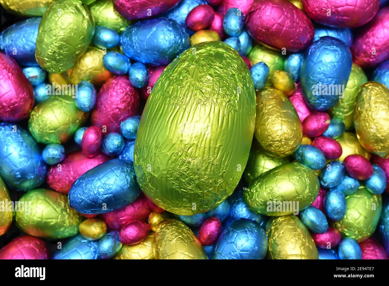 Pile or group of multi colored and different sizes of colourful foil wrapped chocolate easter eggs in pink, blue, yellow and lime green with a large g Stock Photo