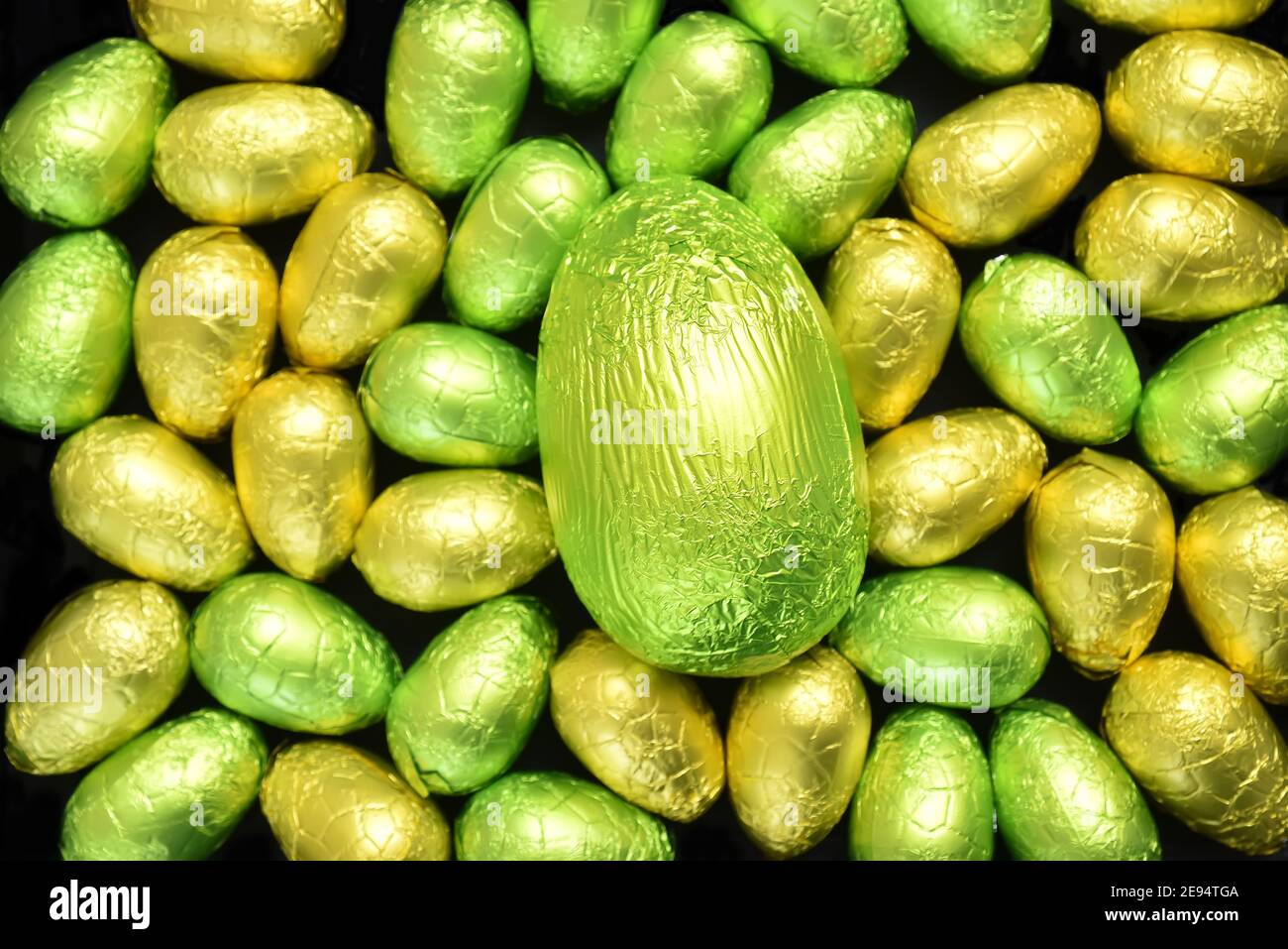 Pile or group of multi colored and different sizes of colourful foil wrapped chocolate easter eggs in yellow and lime green with a large green egg in Stock Photo