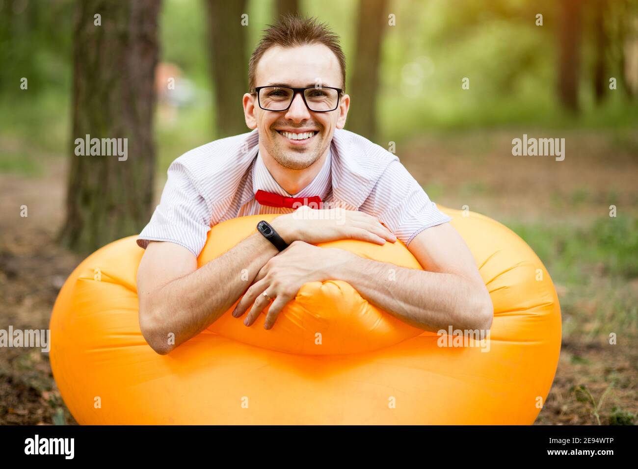 Handsome young man in glasses lying on inflatable yellow sofa and resting in summer park Stock Photo