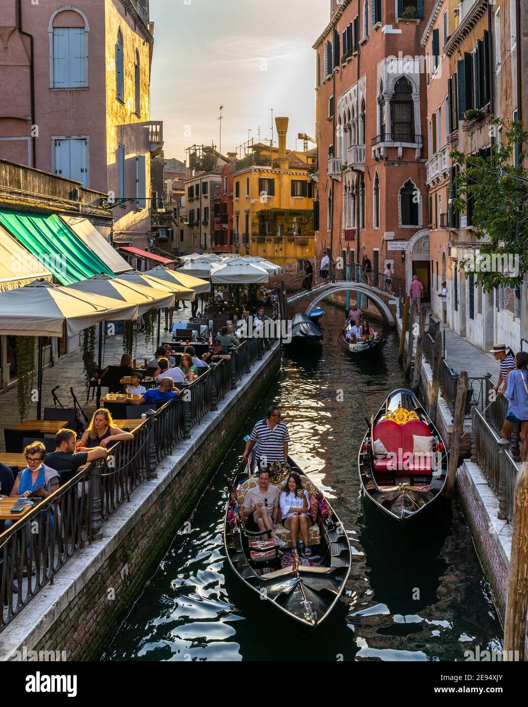 Venice, Italy, Sept. 11, 2020 – Picturesque Venice canal with gondolas and tourists on the right enjoying the sunset in a cocktail bar Stock Photo